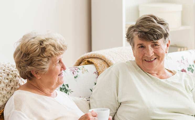 Panoramic view of happy seniors sitting on a couch in care center and looking at their nurse