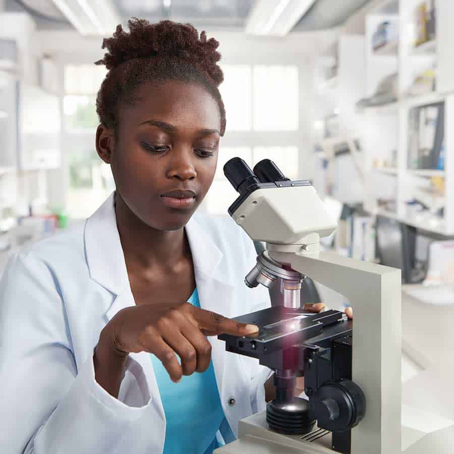 African-american female scientist, student or tech in lab coat works in modern laboratory with a microscope