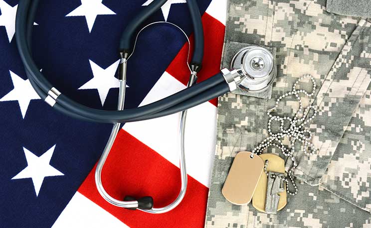 Military fatigues and dog tags on an American Flag with a stethoscope to illustrate health care in the armed services. Horizontal format, fills the frame.
